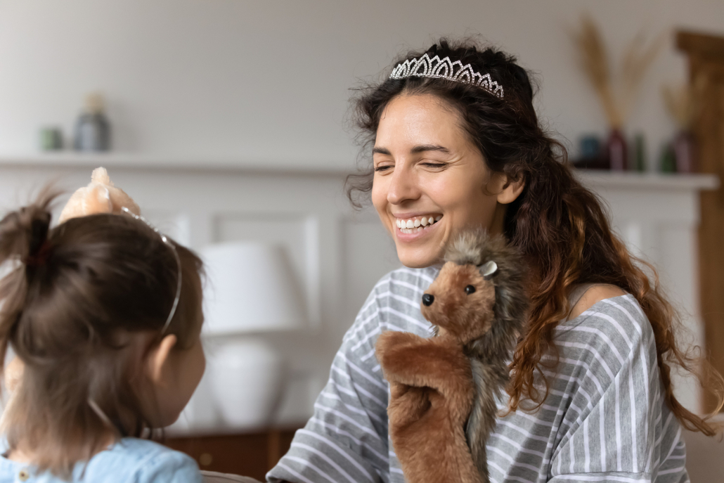 Mother wearing tiara and smiling playing with a puppet with daughter. Communicate through play with your children. Learn how to do this with the help of a play therapist. Online play therapy in Florida is just as effective as in person play therapy. Try working with us in therapy today!