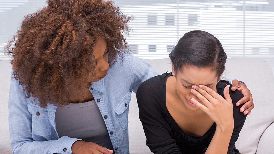 Black woman comforting crying woman on couch. Whether its complex trauma, secondary trauma, or medical trauma, it can leave us stuck. Move forward in PTSD treatment and trauma therapy in Florida for relief.