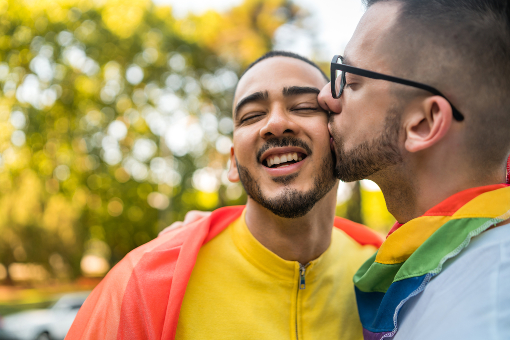 Happy male couple at pride kissing and celebrating. If you're seeking a safe space and freedom, our lgbtq therapists are here to help. Begin LGBT counseling today for further support!