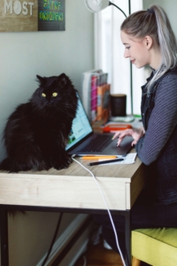 Woman on computer with black cat nearby. Dealing with unprocessed trauma is challenging. Begin EMDR therapy in Florida and see how we can work with you in anxiety treatment, PTSD treatment and trauma therapy, via online therapy in Florida here. Call now for support!