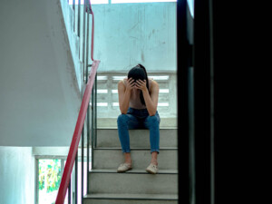Teen sitting on stairs with head in hands. Needing support is ok, but for teens therapy for teens in Florida is best done as early as possible. We can help with anxiety treatment, eating disorders, depression, self-harm, trauma and more. Call now for online therapy!