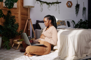 Woman pregnant on laptop. Are you feeling mom guilt or as if you are an overwhelmed mom? Then therapy for new moms in Florida can help. Learn more and begin online therapy when you're ready. 