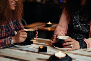 Two friends smile while taking and enjoying coffee together. This could represent the support a trauma therapist in Florida can offer via online therapy in Florida. Learn more about stress therapy in Florida and other services that can support you today.