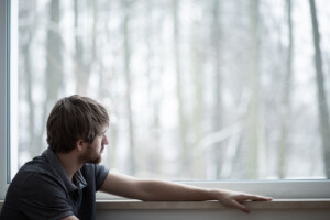 A man sits next to a a window while looking out at a forest. Online therapy in Florida can help you overcome emotional issues from the comfort of home. Learn more about stress therapy in Florida by contacting a trauma therapist in Florida today.