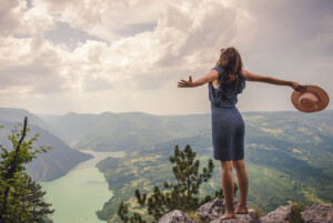 A woman raises her arms in joy while standing out over a valley and river. This could represent overcoming past trauma with the help of a trauma therapist in Florida. Learn more about the support eating disorder treatment can offer today.
