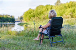A person sits in a chair near a lake while appreciating the nature around them. Learn how online therapy in Florida can offer support from where is most convenient. Contact a trauma therapist in Florida to learn more today.