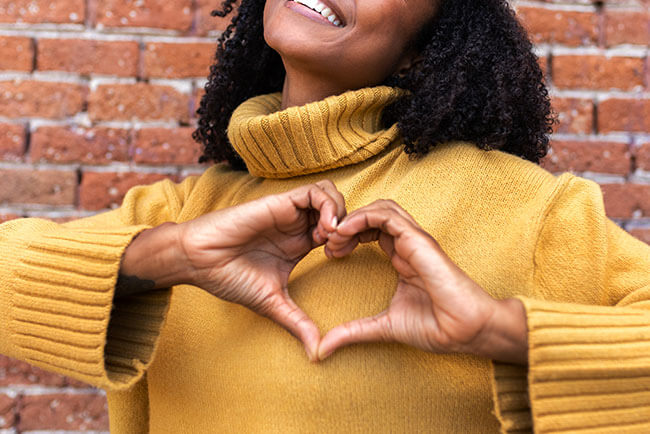 Woman making a heart shape with her hands. If you're struggling to display self love, then online coaching in Texas or florida can help. Online coaching for women is a great way to discover yourself with a skilled self-love coach. Get in touch for more information.