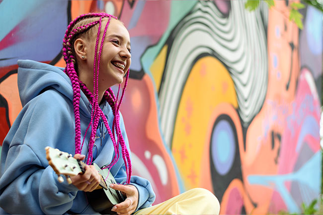 Smiling teenager with bright purple hair playing a guitar
