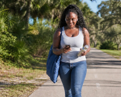 Young woman walking on a paved path while talking on her smart phone depicting virtual walk and talk therapy in Florida