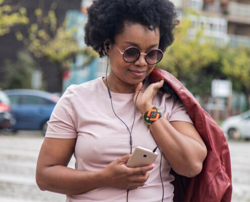 Young Hispanic Woman wearing earbuds and having a private conversation on her phone. This represents a very common way for a person to enjoy virtual walk and talk therapy.