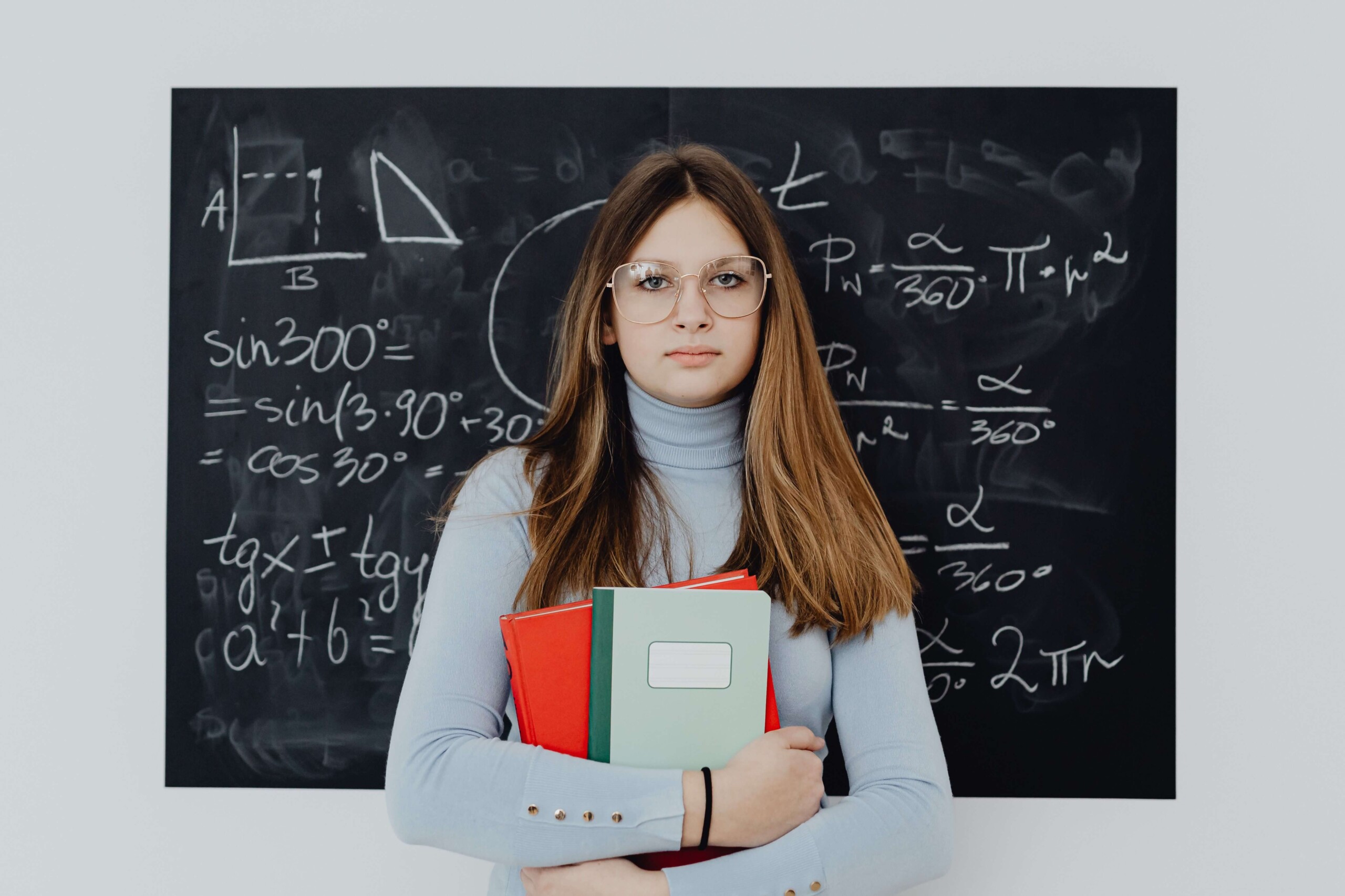 A teen girl holds a stack of notebooks while standing in front of a chalkboard. Masking at school to keep up appearances can quietly wear a teen down over time. A neurodivergent-affirming therapist for teens in Merritt Island, FL can help your child feel safe being themselves.