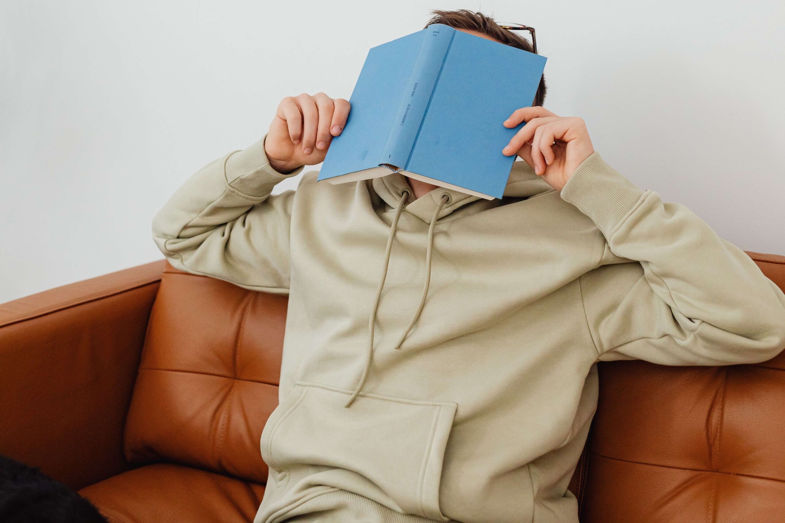 A young man sits on a couch, holding a blue book up to hide his face. Masking often shows up as exhaustion or withdrawal once your teen gets home. A neurodivergent-affirming therapist for teens in Merritt Island, FL can help your teen navigate this pattern with support.