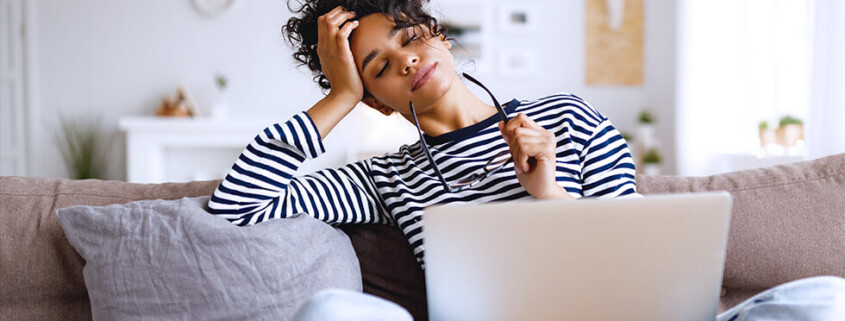 Woman on a couch with her laptop pauses to reflect on what she's read
